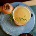 smoked persimmon cocktail with a persimmon and rosemary on a blue ceramic cheese plate