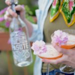 bottle of tequila with two coupe glasses and cherry blossoms for garnish