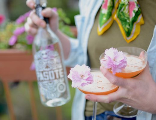 bottle of tequila with two coupe glasses and cherry blossoms for garnish