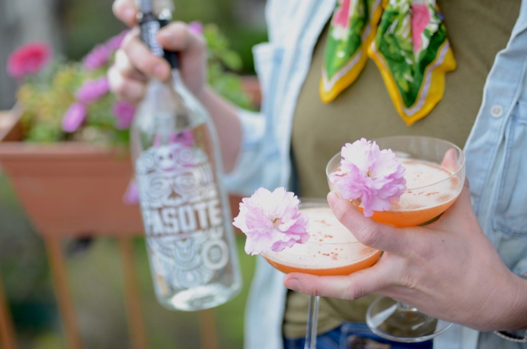 bottle of tequila with two coupe glasses and cherry blossoms for garnish